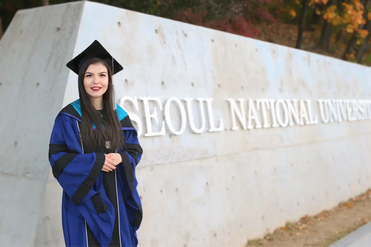 Tahmina in her graduation gown beside the Seoul National University sign.